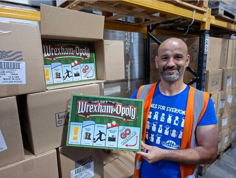 Danny at the Cheatwell Warehouse holding a copy of a new Outset Media board game called Wrexham-Opoly