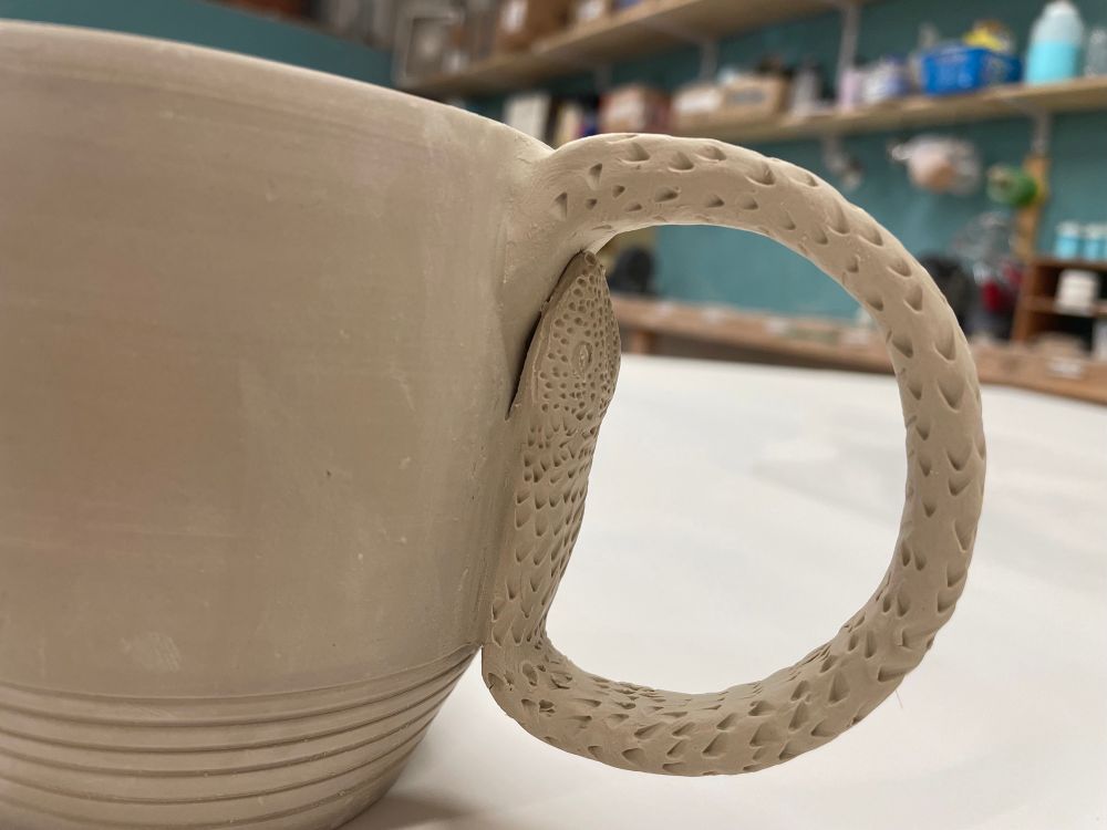 Close up of mug handle sculpted to look like a snake with textured skin. 