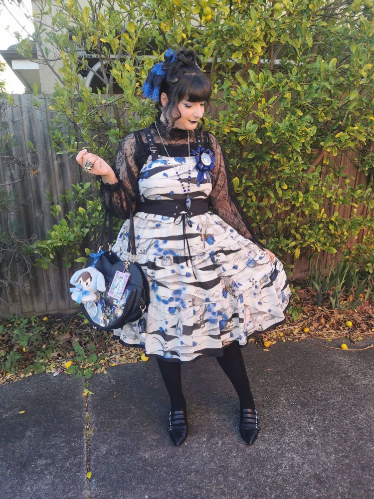 Picture of a woman (me) showing off her outfit. The main dress is mostly white and blue and she's coordinating it with black. I'm also holding an ita bag.