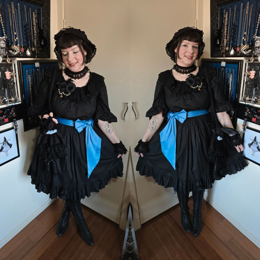 Two images combined into one. Both images are of a woman (me) posing showing off her black outfit with a blue waist tie. 
On the wall behind her, there are frames with jewellery hanging. 