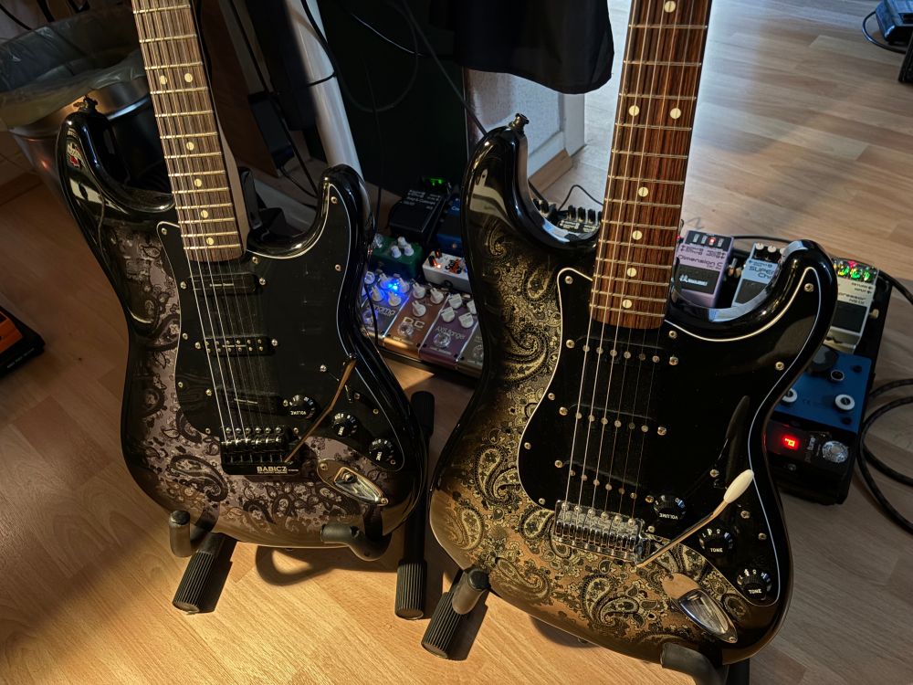 Zwei Fender Statocaster Gitarren mit Paisley-Muster vor einem Pedalboard.