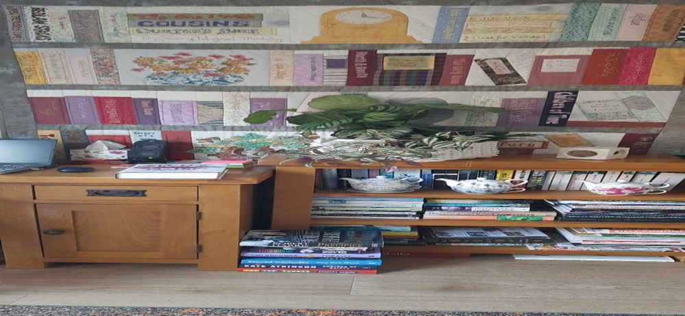 A bookcase and behind it, a quilt made to look like a bookcase.  All the books I read in 2018.  Read a book, make a spine!