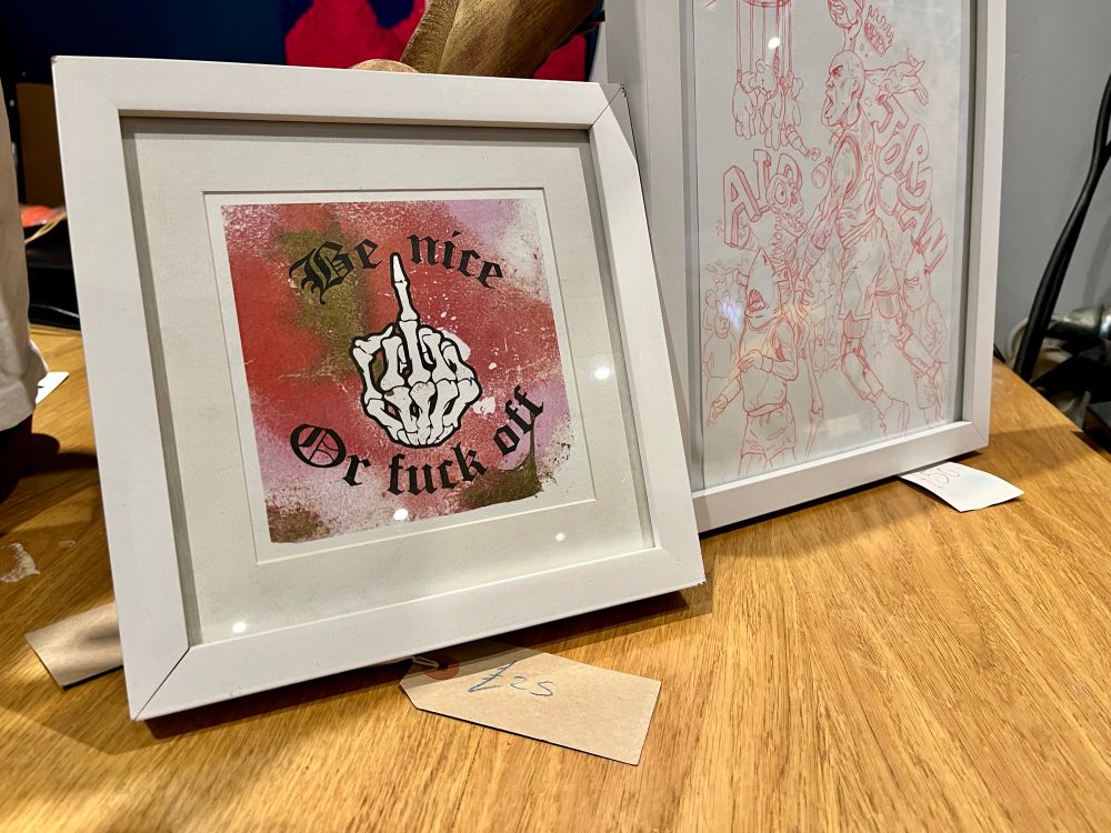 A framed picture of a skeleton hand showing its middle finger with the text “Be nice or fuck off”. 