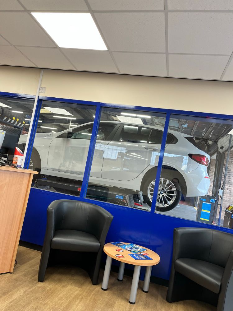 A waiting room with a glass window through which can be seen a white car in mid air