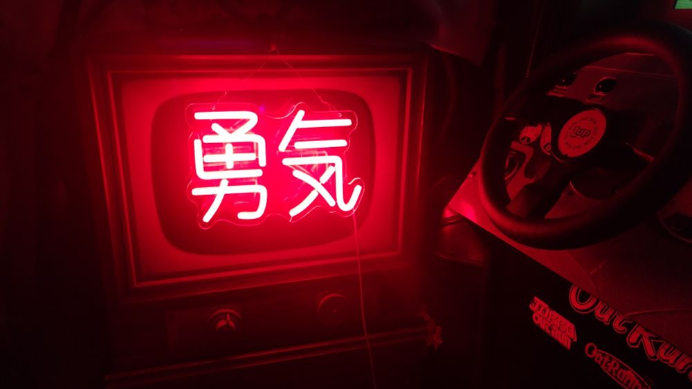 an old tv screen with neon kanji overtop it. a racing arcade machine to the right