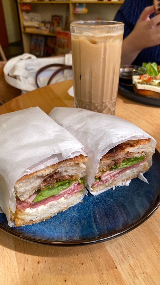 Meat sandwich on a blue plate plus a tall glass of spanish latte