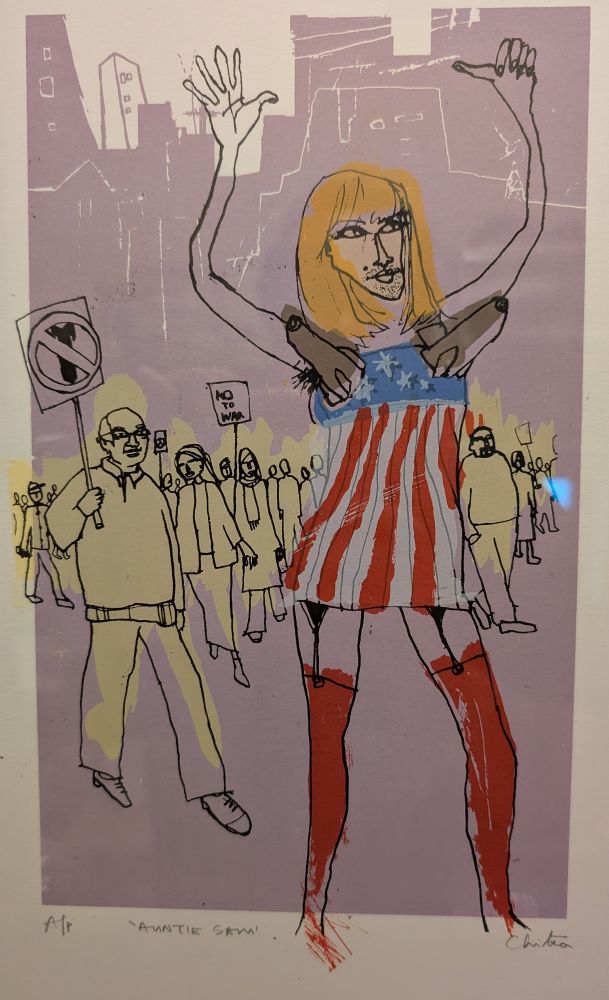 A print by Chitra Merchant of an Iraq invasion protest with "Auntie Sam" in the foreground wearing a missile bra and an Old Glory dress.