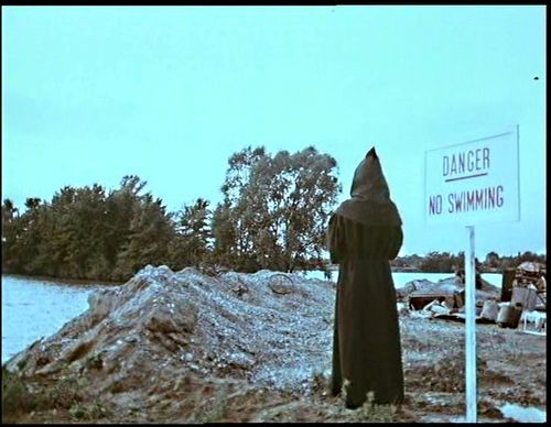 The spirit of dark and lonely waters stands next to a sign reading: "Danger. No Swimming."