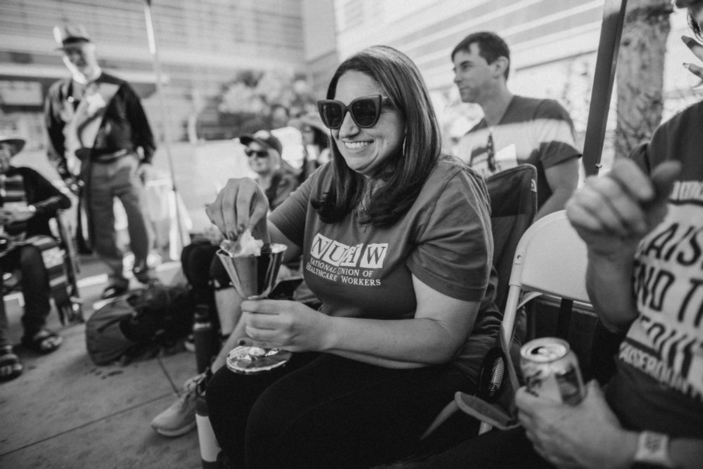 4/11: Members of NUHW, Kaiser Permanente's mental healthcare union, break a 5-day hunger strike. A smiling member dips bread into a cup of wine as a fast-breaking ceremony guided by clergy from CLUE. (BW)