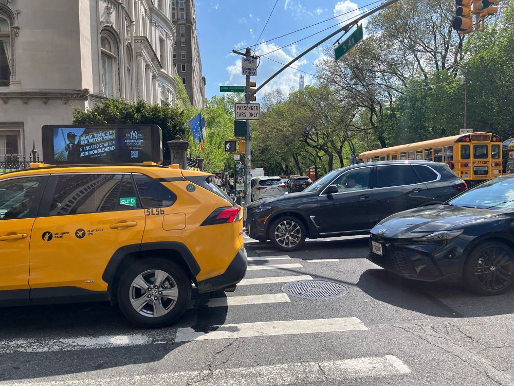 Same intersection, opposite light cycle: drivers of several other cars, plus a taxi, running a red light and blocking a crosswalk, which, if they were riding bikes would land them in court. 