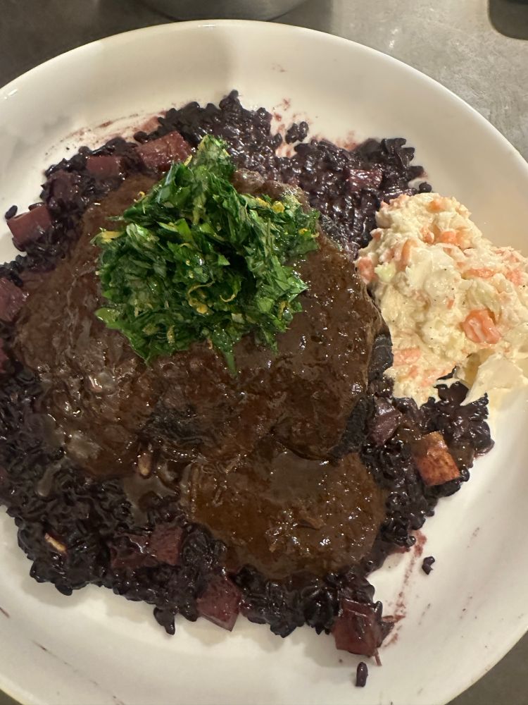 A plate of black rice risotto and beef cheeks with cold slaw. 
