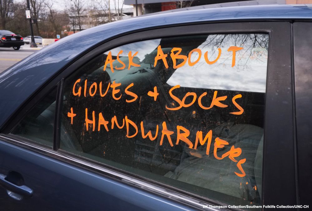 “Ask About Gloves & Socks & Handwarmers” marked on car window parked near mutual aid organization, Hillsborough St., Raleigh NC, Dec. 23, 2023. DK Thompson Collection/Southern Folklife Collection/UNC-CH