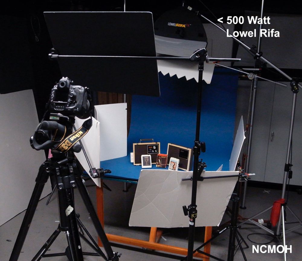 tabletop set for artifact grouping using a soft light to the top back, kicked forward at an angle to camera. white cards act as reflectors for fill light. the serrated card under the light is feathering a shadow that is cast onto the background to create gradation. the black in front of the camera is blocking light hitting the lens. 