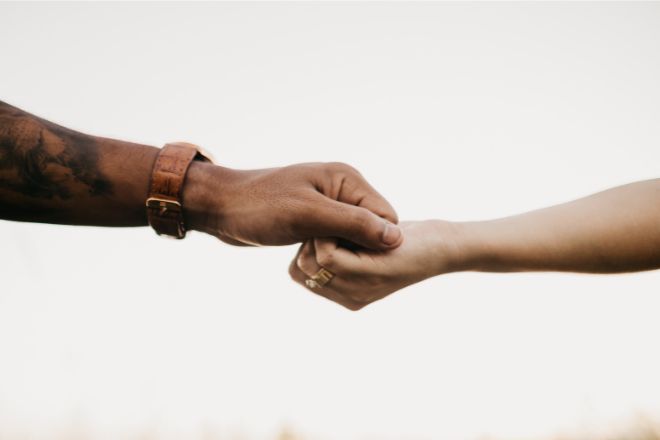 Photo of a global majority person's hand holding a white woman's hand - Photo credit Canva