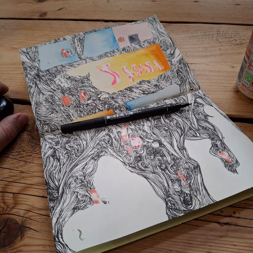 A sketchbook open on a wooden table. The pages are mostly filled with busy, squiggly black linework 
