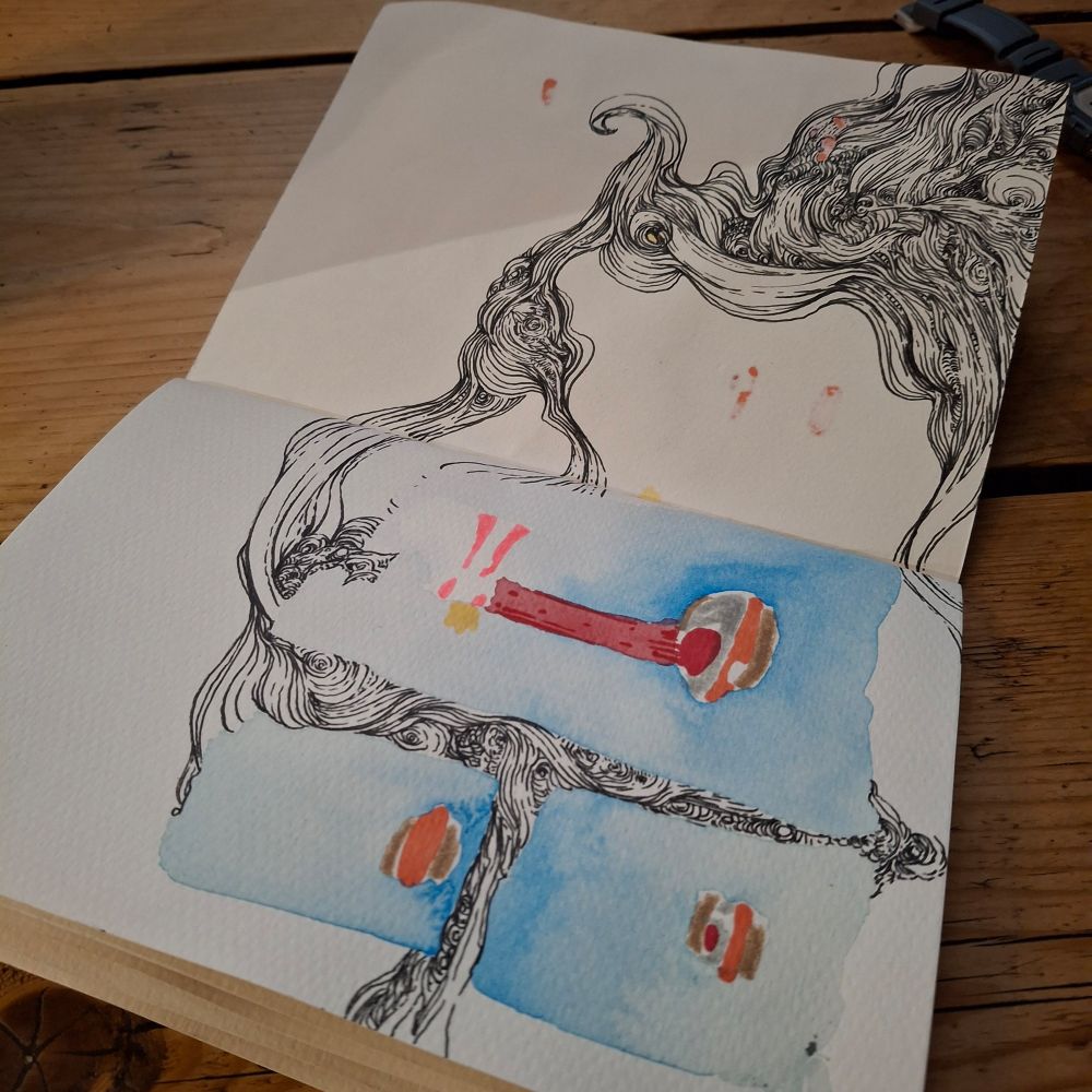 A sketchbook open on a wooden table. On one page are three blue watercolour rectangles with orange and brown shapes inside. Both pages have squiggly black linework.
