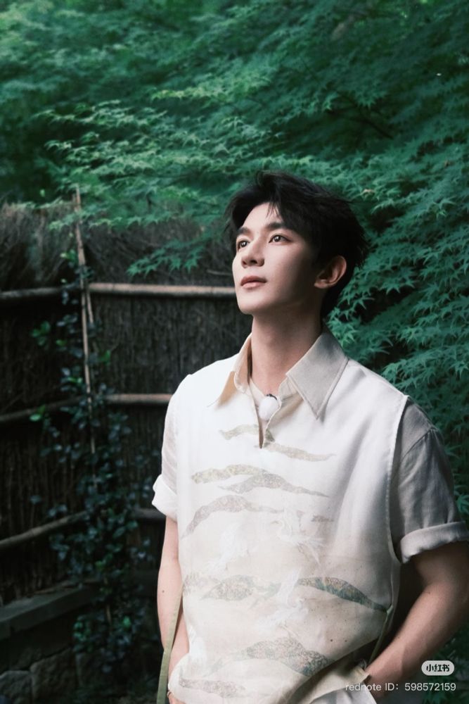 xia zhiguang standing in front of lush greenery in a white shirt with a crane print. 