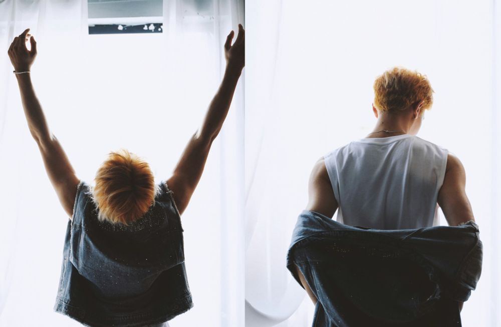 two images of xia zhiguang from behind with blonde hair standing in front of bright light in a light wash sleeveless denim jacket and white shirt, on the left with his arms raised and on the right with the jacket lowered to his elbows. 