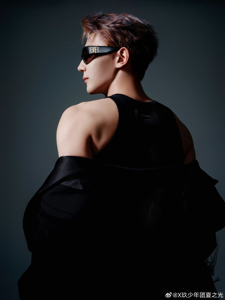 xia zhiguang from behind with his head turned in profile wearing black sunglasses and a black jacket pulled down to expose his shoulder. 