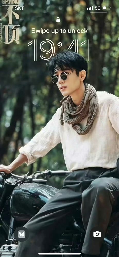 screenshot of a phone lock screen with xiao zhan as ren shaobai sitting on a motorcycle wearing round sunglasses. 