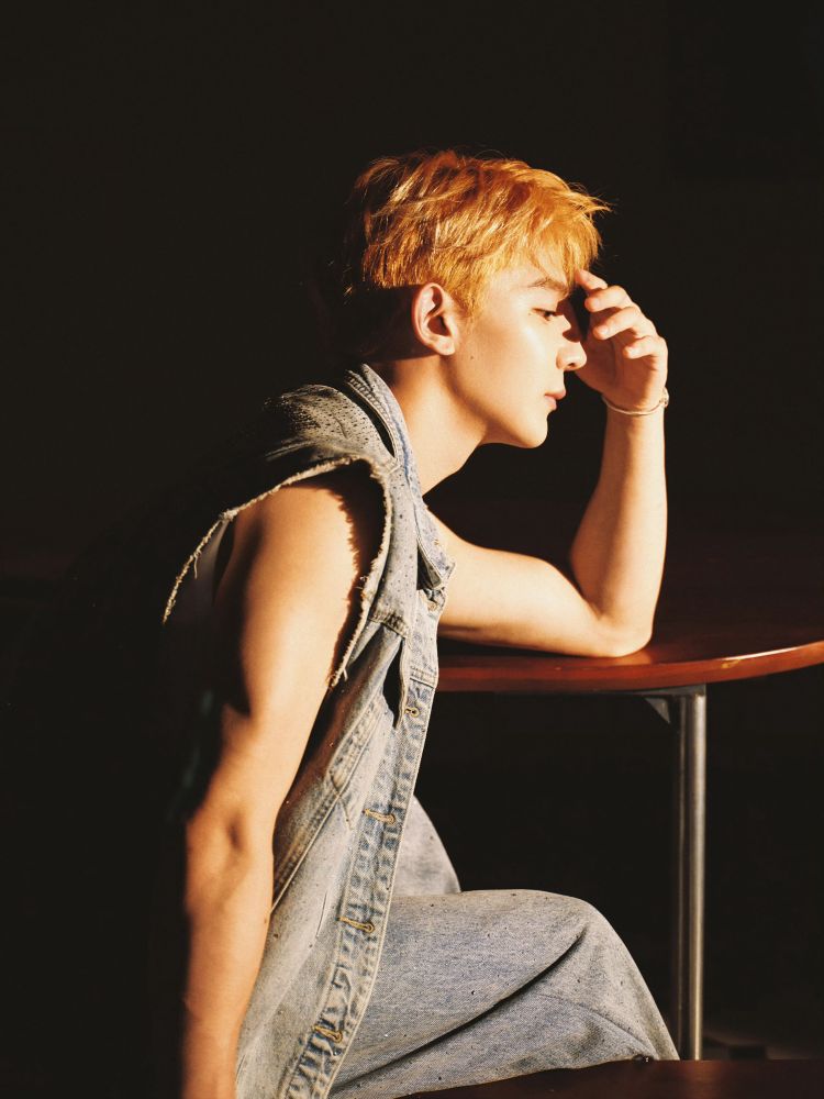 xia zhiguang in profile with warm light hitting his face while he leans against a table. 