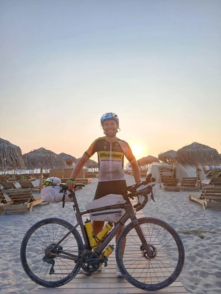 Ein Bild von Christoph Strasser mit seinem Fahrrad am Strand des Schwarzen Meeres. Im Hintergrund geht die Sonne auf. 