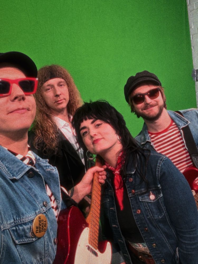 Die Band steht vor einem Greenscreen und lächelt frontal in die Kamera.