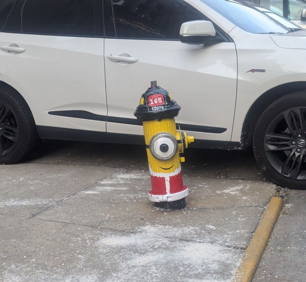 A fire hydrant painted to look like a minion wearing a Santa costume for Christmas. 