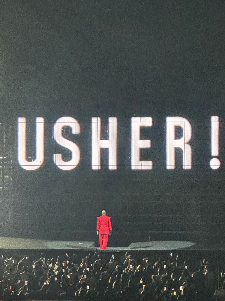 A picture of Usher standing in front of a graphic that says “Usher!”