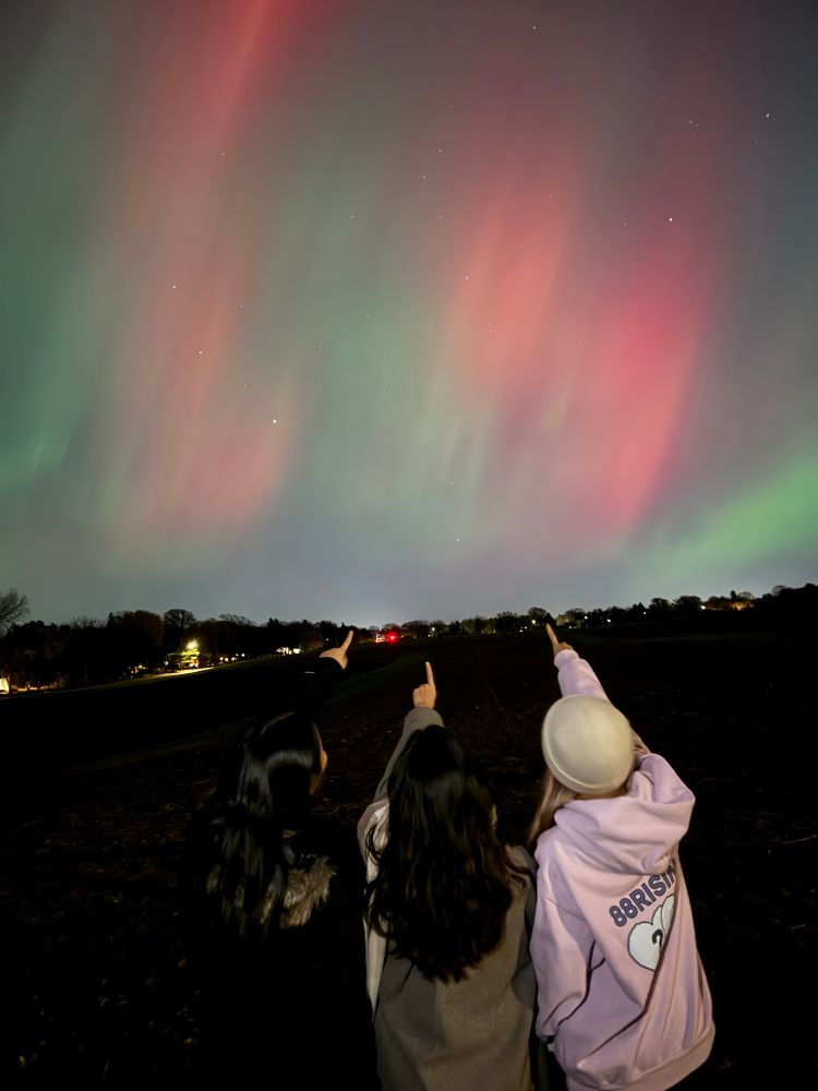 Three people pointing at the northern lights in the sky 