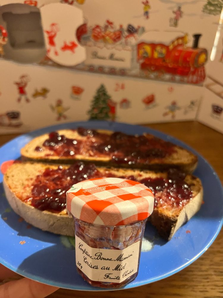 A Bonne Maman Cherry with Honey jam mini jar, with toast and advent calendar behind 