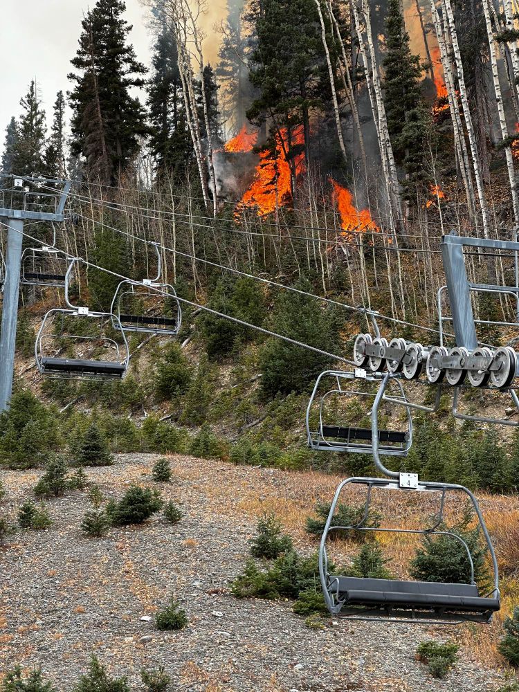 Piles of woody debris burn behind an empty ski lift