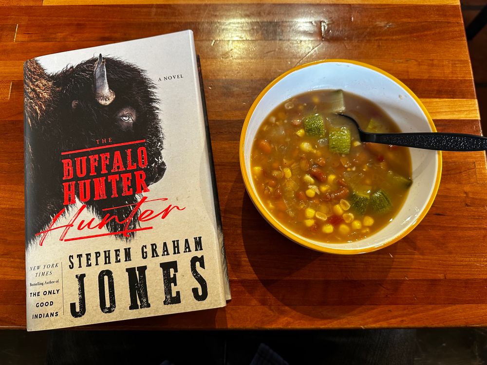 The book “The Buffalo Hunter Hunter” by Stephen Graham Jones next to a bowl of soup.