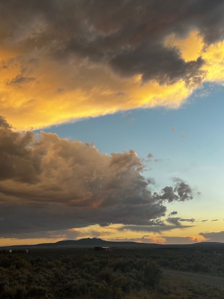 A yellow sunset over a mesa and a mountain in the distance  with large clouds in the sky.
