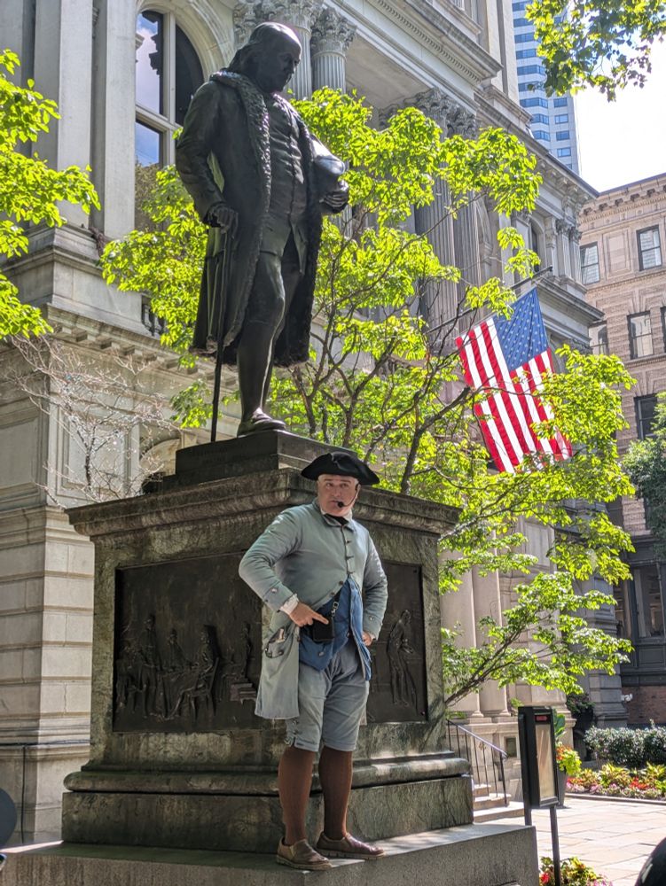 A costumed Freedom Trail Player standing in front of a statue of Ben Franklin.