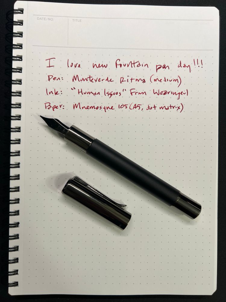 A matte black fountain pen laying parallel to its cap at a 45 degree angle on top of dot matrix paper. On the paper, written in red ink, reads:

I love new pen day!!!
Pen: Monteverde Ritma (medium)
Ink: “Human Issues” from Wearingeul
Paper: Mnemosyne 105 (A5, dot matrix)