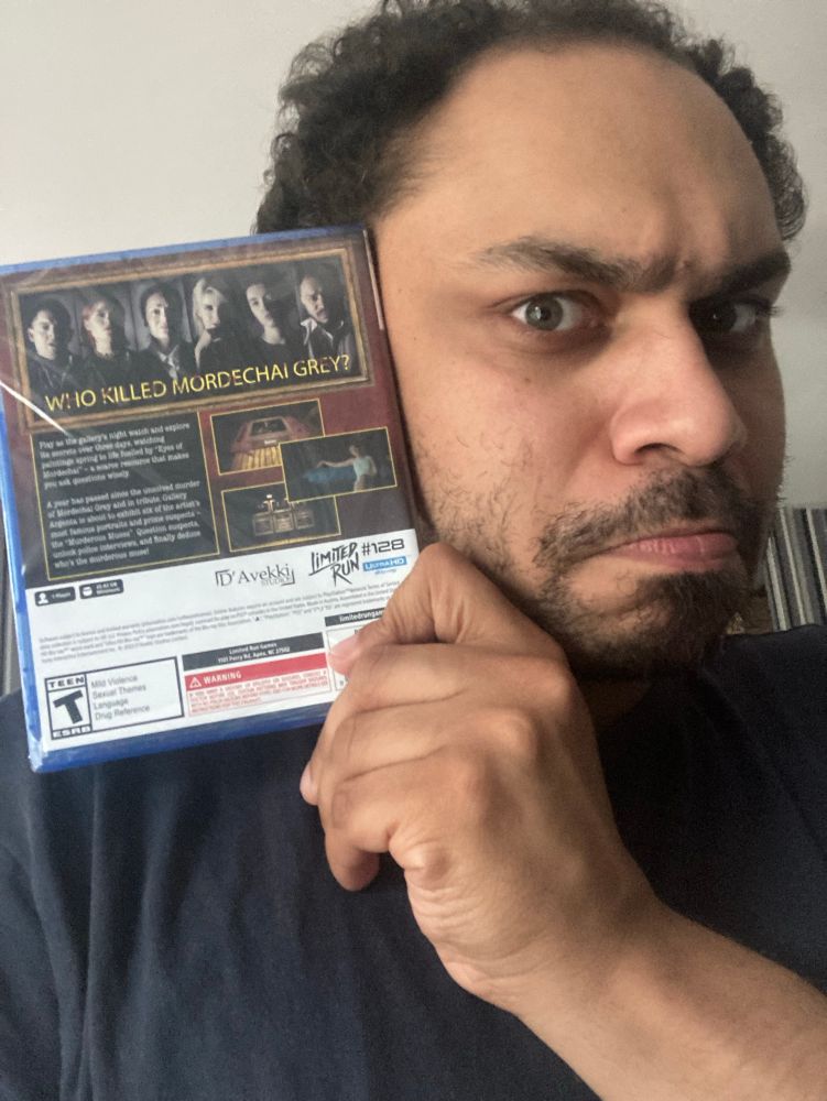 Me, more sternly, holding my copy of Murderous Muses for the PS5!