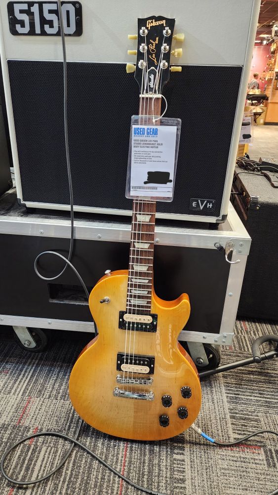 A picture of a Gibson Les Paul at a Guitar Center, leaning against a 5150 amplifier. The Les Paul has a polished wood finish body called "lemonburst".