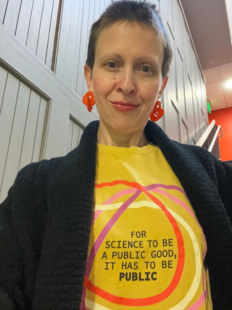 A person wearing a yellow T-shirt that reads: For science to be a public good, it has to be PUBLIC.