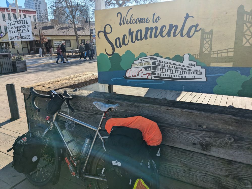 My touring bike leaning against a welcome to Sacramento sign on the boardwalk
