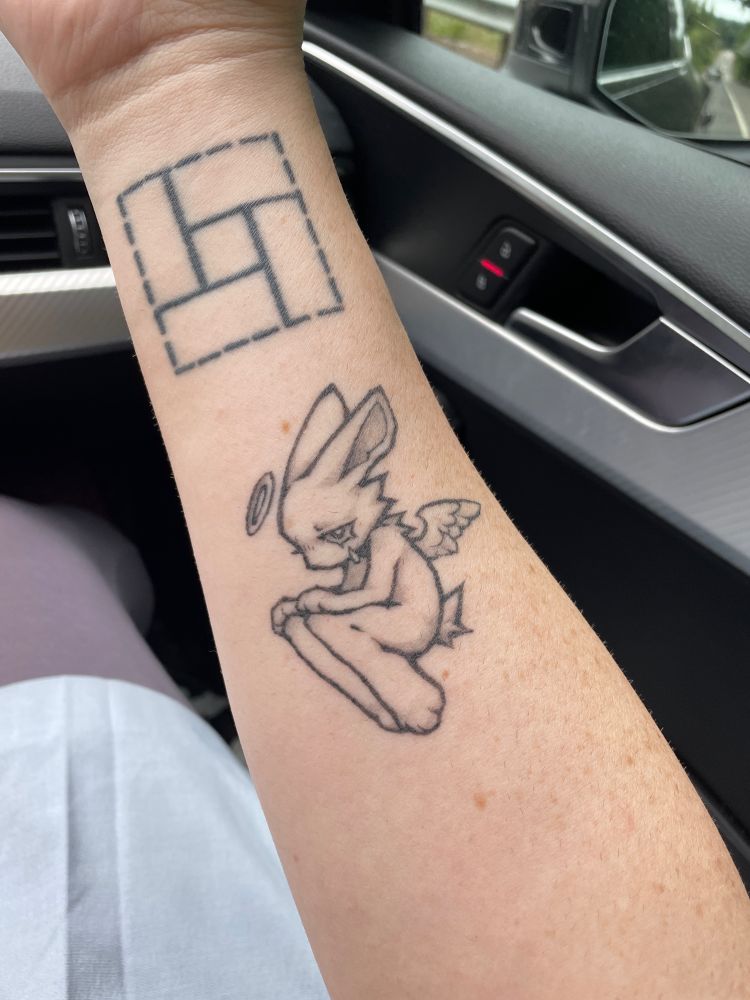 A tattoo on the inside of a forearm. The tattoo depicts a kemo-style rabbit, floating with its hands on its knees. It has angel wings and a halo, and is shedding a single tear.