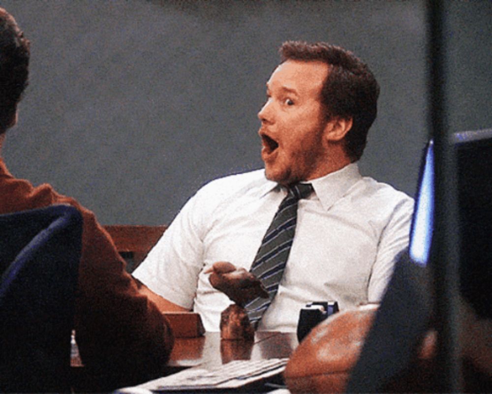 a man in a white shirt and tie is sitting at a desk with his mouth open