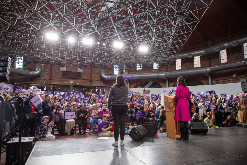 Michelle Wu stands at a podium in front of hundreds of supporters waving Mayor Wu signs.