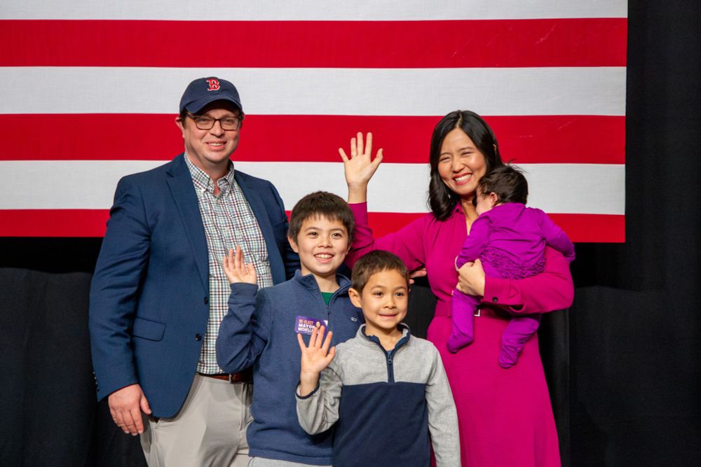 Photo of Mayor Michelle Wu waving with her husband, Conor Pewarski, and three kids, Blaise, Cass, and Mira.