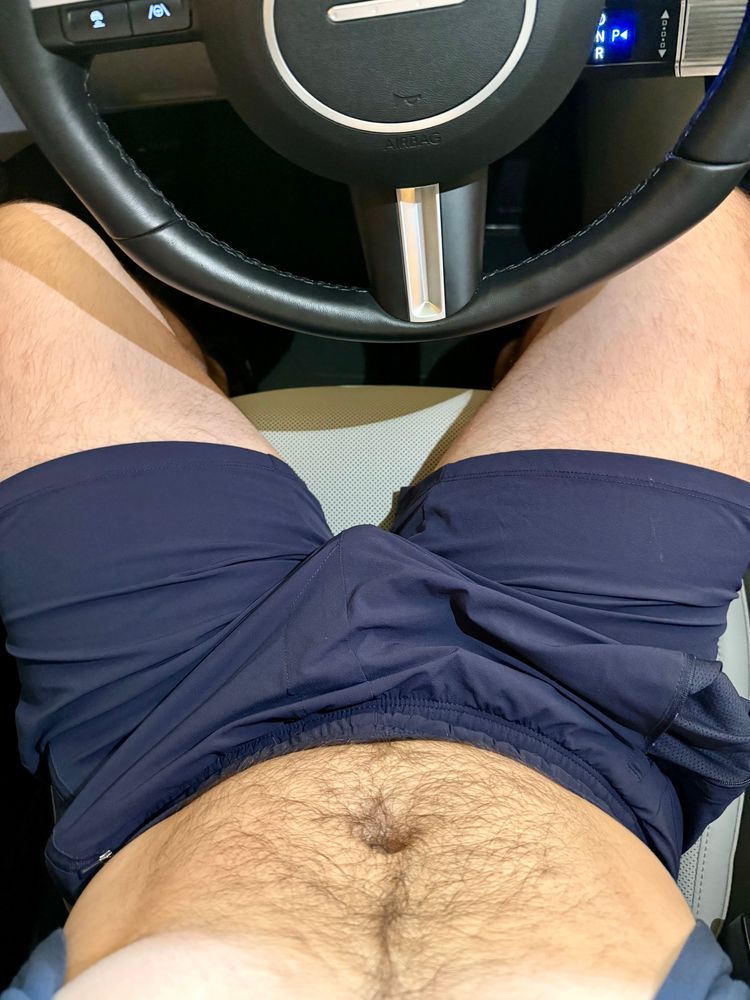 Sitting in my parked car with my shirt pulled up showing my hairy belly and dark blue gym shorts.