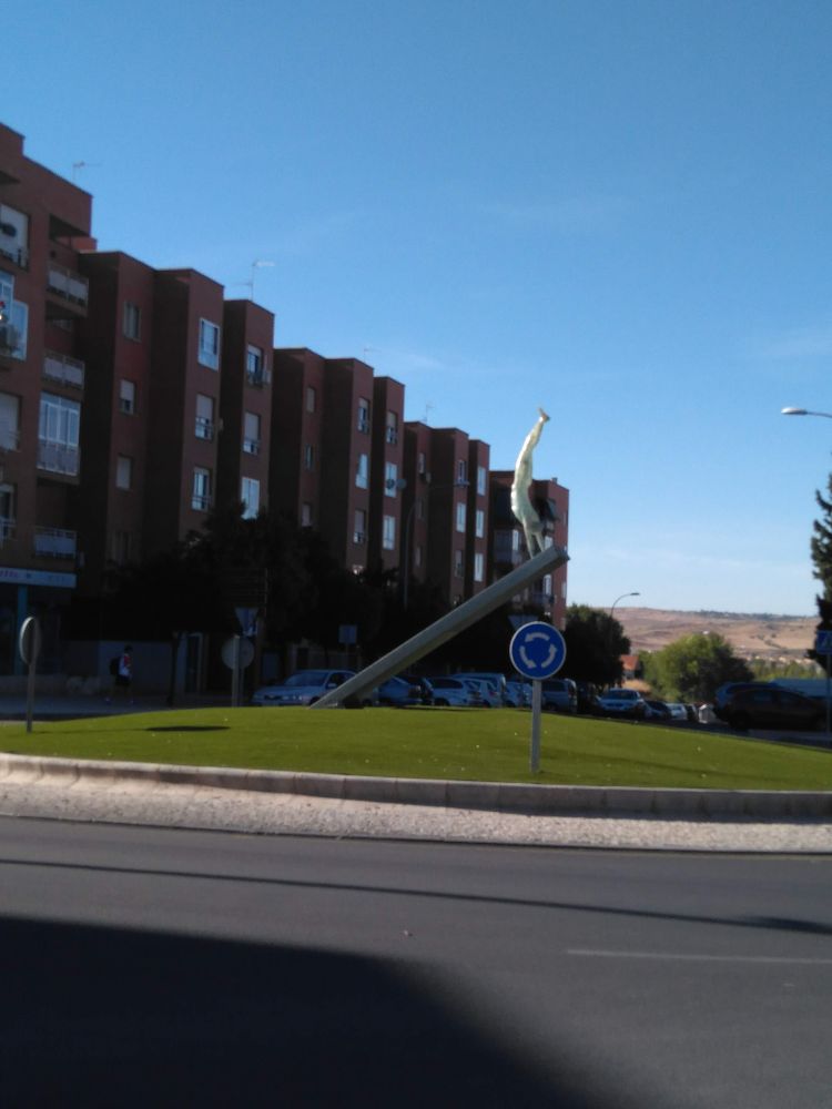 Sobre una barra inclinada hay una escultura de un material translúcido que se sostiene de pie sobre las manos