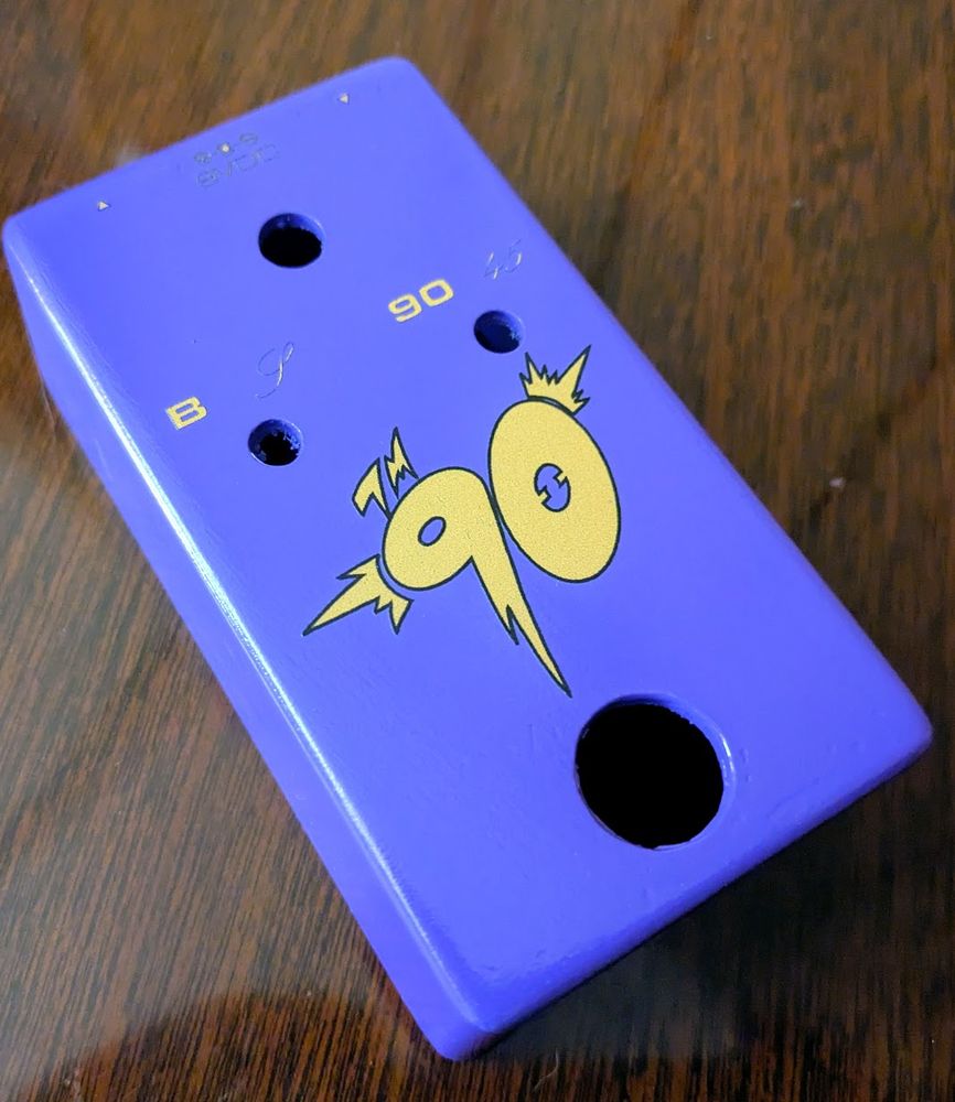 A purple guitar pedal enclosure, with UV painted designed. The main image is a large stylized "90."