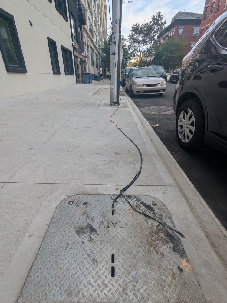 A cable coming out of a cable handhold and snaking up a utility pole
