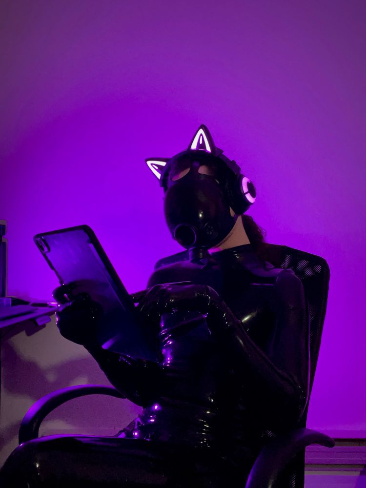 Designer, clad in latex, gas mask and headphones sitting in their chair. Fiddling with the tablet in front of them meticulously. 