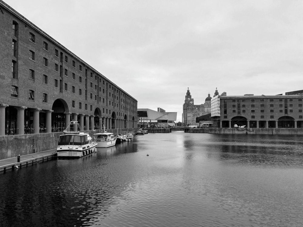 Vista del muelle de Liverpool desde el Royal Albert Dock, al fondo el Museo de la Ciudad y más allá el emblemático edificio Royal Liver Building con los dos pájaros que coronan sus torres. Foto en blanco y negro tomada con el móvil.